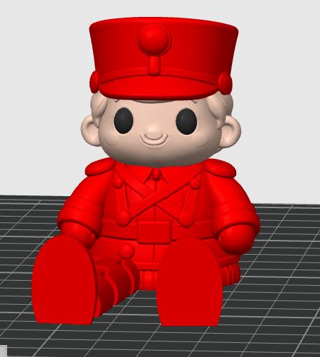 May include: A 3D digital model of a seated figure wearing a bright red military-style uniform with a matching red cap. The figure has a light-colored face, round black eyes, and a simple smiling mouth, rendered against a dark gray grid background.