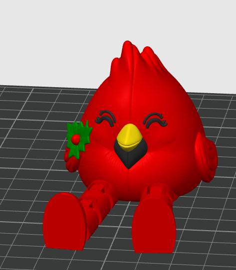 May include: A bright red cardinal figurine with a yellow beak, black eyes, and a green holly leaf accent on the side of its head. The bird has a rounded body, a pointed crest, and two articulated legs extending forward in a seated position.