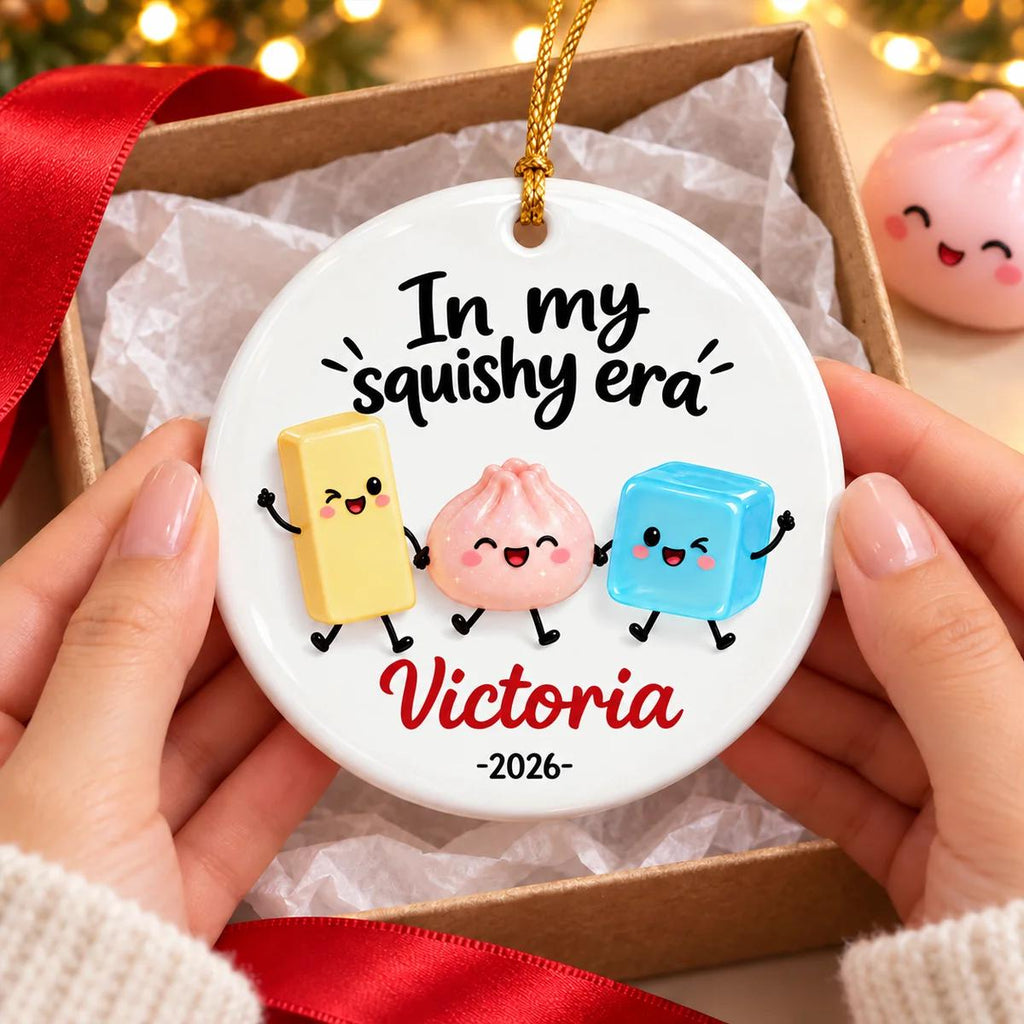 May include: A round white ceramic ornament featuring the black text In my squishy era, a yellow rectangular character, a pink dumpling character, and a blue cube character. The name Victoria and the year 2026 are printed in red and black below.