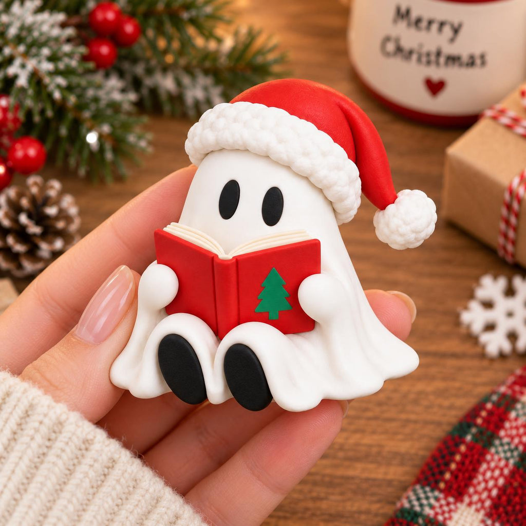 May include: A small white ghost figurine wearing a red Santa hat with a white pom-pom and trim. The ghost has black oval eyes, black feet, and is holding an open red book with a green Christmas tree graphic on the cover, crafted in a smooth finish.