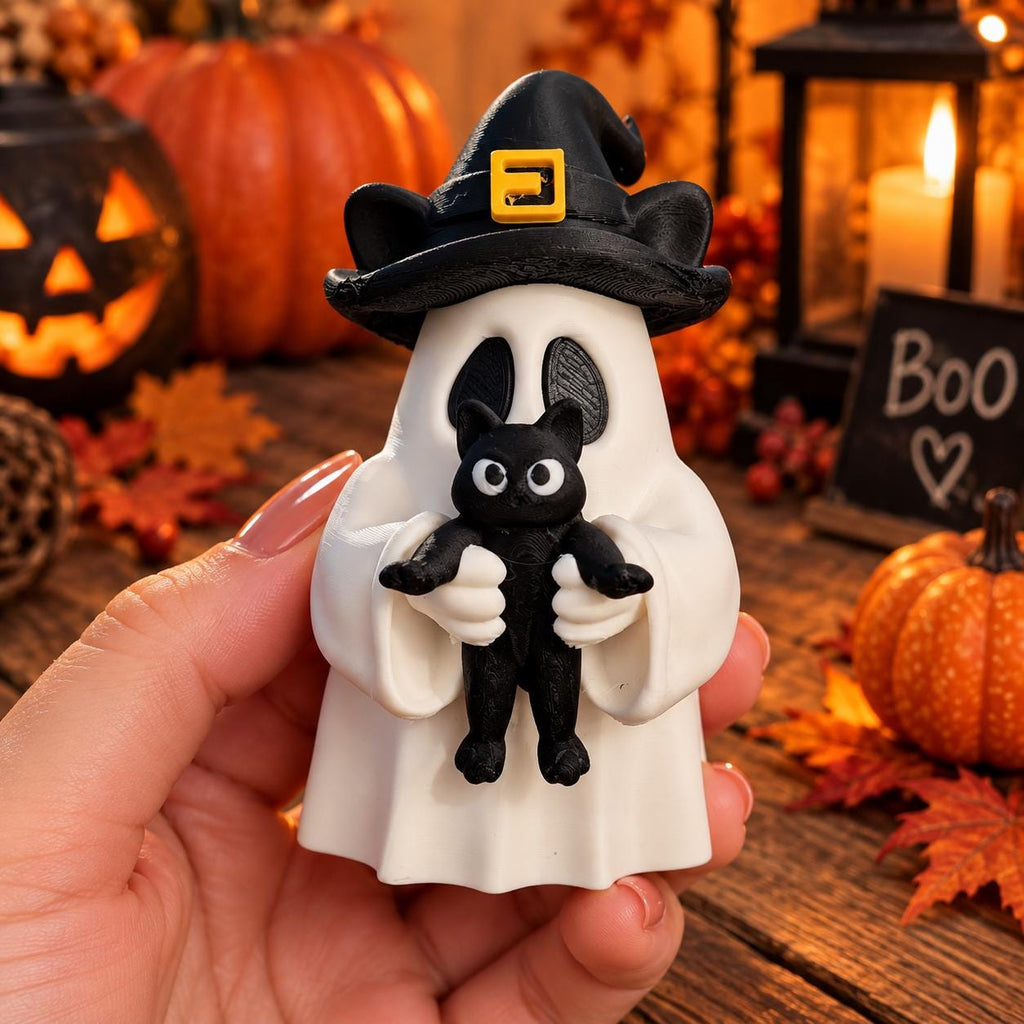 May include: A white ghost figurine wearing a black witch hat with a yellow buckle, holding a small black cat. The ghost has two oval-shaped eye cutouts and is crafted with a smooth finish. The black cat features large white eyes and a simple design.