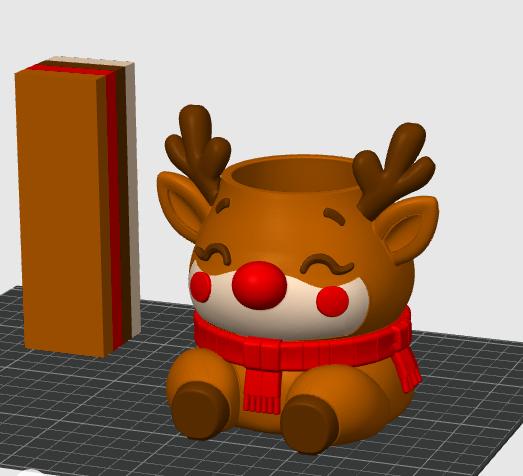 May include: A brown reindeer-shaped planter with a bright red nose, red cheeks, and a red scarf wrapped around its neck. The reindeer has dark brown antlers and closed eyes. Next to the planter is a tall, rectangular block with layered colors.
