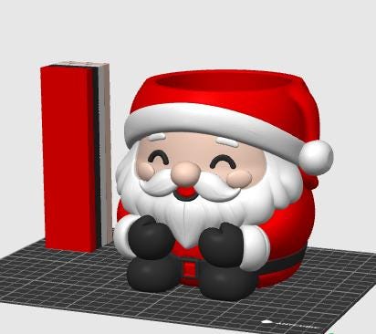 May include: A 3D rendered Santa Claus container featuring a red hat with a white pom-pom, a white beard, black gloves, and a black belt with a red buckle. The figure has a smiling face with closed eyes and is positioned next to a red rectangular block.