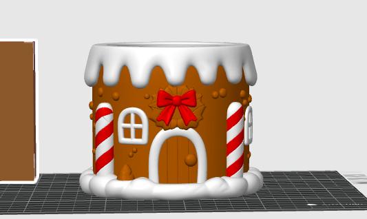 May include: A cylindrical gingerbread house container featuring a brown exterior with white icing trim at the top and bottom. The design includes a central arched doorway, a red bow, two white and red striped candy canes, and white windows.