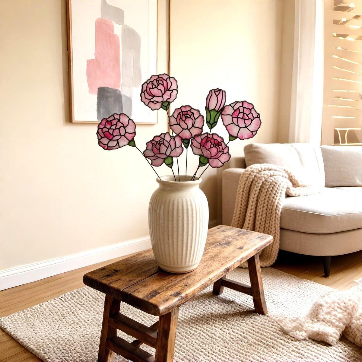May include: A collection of seven stained glass carnations in shades of pink and white with dark outlines, arranged on thin metal stems. The flowers are displayed in a cream-colored, vertically ribbed ceramic vase with a rounded body.