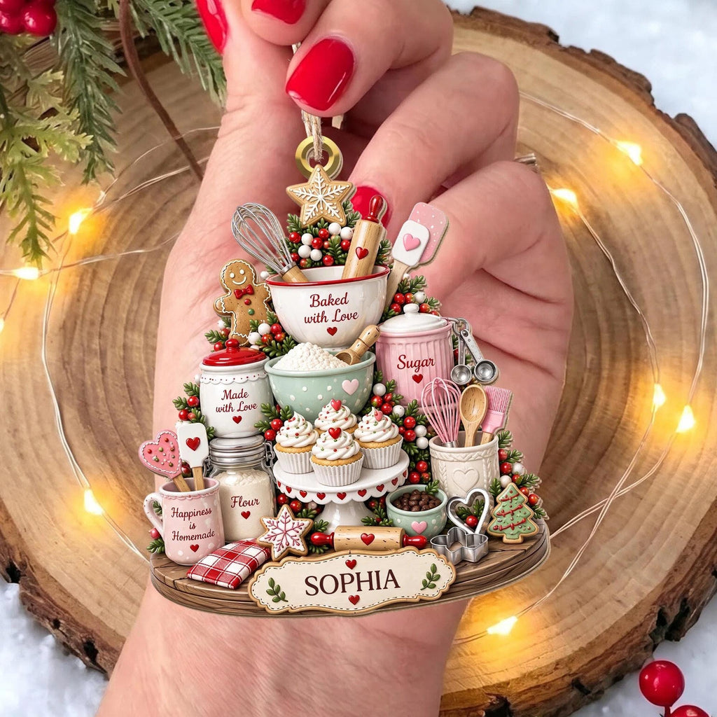May include: A decorative Christmas ornament shaped like a baking scene, featuring miniature kitchen items like a whisk, rolling pin, cupcakes, and jars labeled Made with Love, Sugar, and Flour. The base includes a plaque with the name SOPHIA.