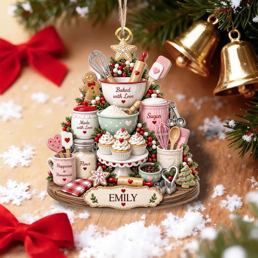 May include: A decorative Christmas tree ornament shaped like a baking scene with a gingerbread person, mixing bowls, cupcakes, and kitchen tools. The ornament features text including Baked with Love, Made with Love, Sugar, Flour, Happiness is Homemade, and EMILY.