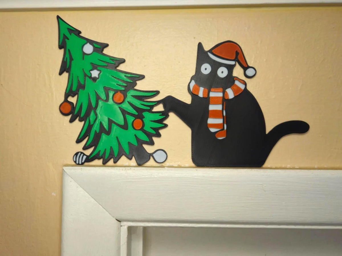May include: A flat decorative cutout featuring a black cat wearing an orange and white striped hat and scarf, reaching out with one paw toward a green Christmas tree decorated with orange ornaments and white star-shaped accents.