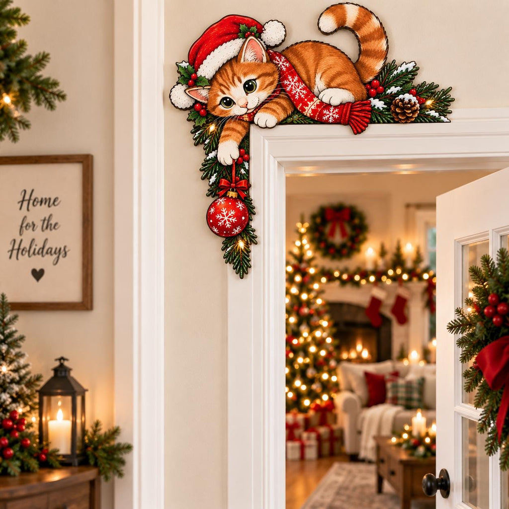 May include: A decorative wooden door corner sign featuring an orange tabby cat wearing a red Santa hat and a red scarf with white snowflakes. The cat is perched on green pine branches with red berries and a pinecone, holding a red Christmas ornament.