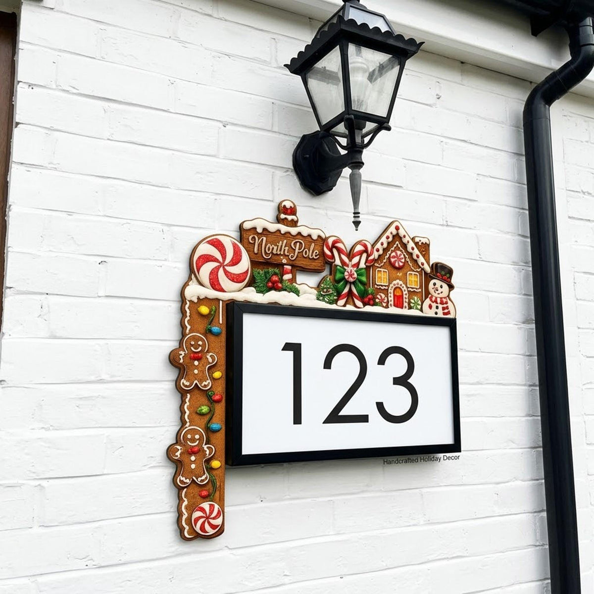May include: A rectangular house number sign displaying the digits 123 in black on a white background. The frame is decorated with gingerbread-themed accents, including a North Pole sign, candy canes, a gingerbread house, and gingerbread men.