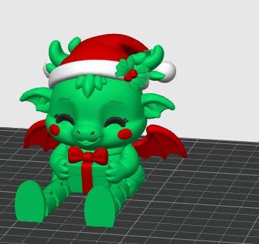 May include: A green dragon figurine wearing a red and white Santa hat with holly leaves and berries. The dragon has small red wings, red circular cheeks, and is holding a green gift box tied with a red ribbon and a red bow on the front.