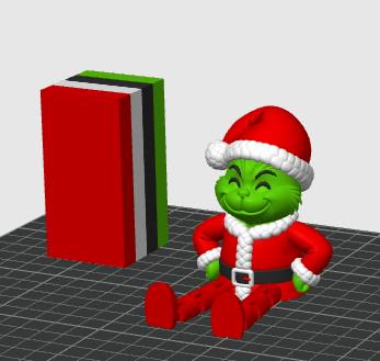 May include: A green character figurine wearing a red Santa suit with white trim and a matching hat, sitting next to a rectangular block composed of stacked layers in red, white, black, and green colors, presented on a dark grid surface.