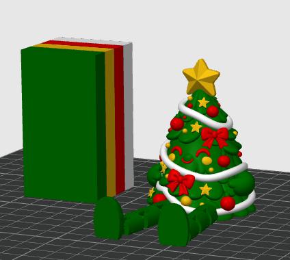 May include: A green Christmas tree figurine with a smiling face, decorated with red ornaments, yellow stars, and red bows, wrapped in a white garland and topped with a yellow star. Beside it stands a rectangular block with green, yellow, red, and white layers.