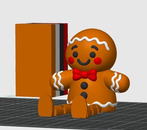 May include: A brown gingerbread person figurine with white icing details, a red bow tie, and two black buttons on the torso. The figure has red circular cheeks, black eyes, and a smiling mouth. Beside it stands a rectangular block with orange, white, black, and red vertical stripes.