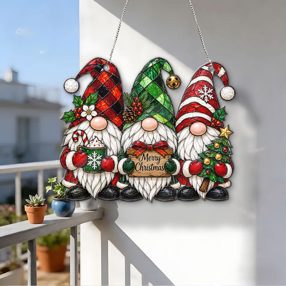 May include: A hanging decoration featuring three gnomes with white beards. The left gnome wears a red plaid hat, the center wears a green plaid hat, and the right wears a red striped hat. The center gnome holds a sign that reads Merry Christmas.