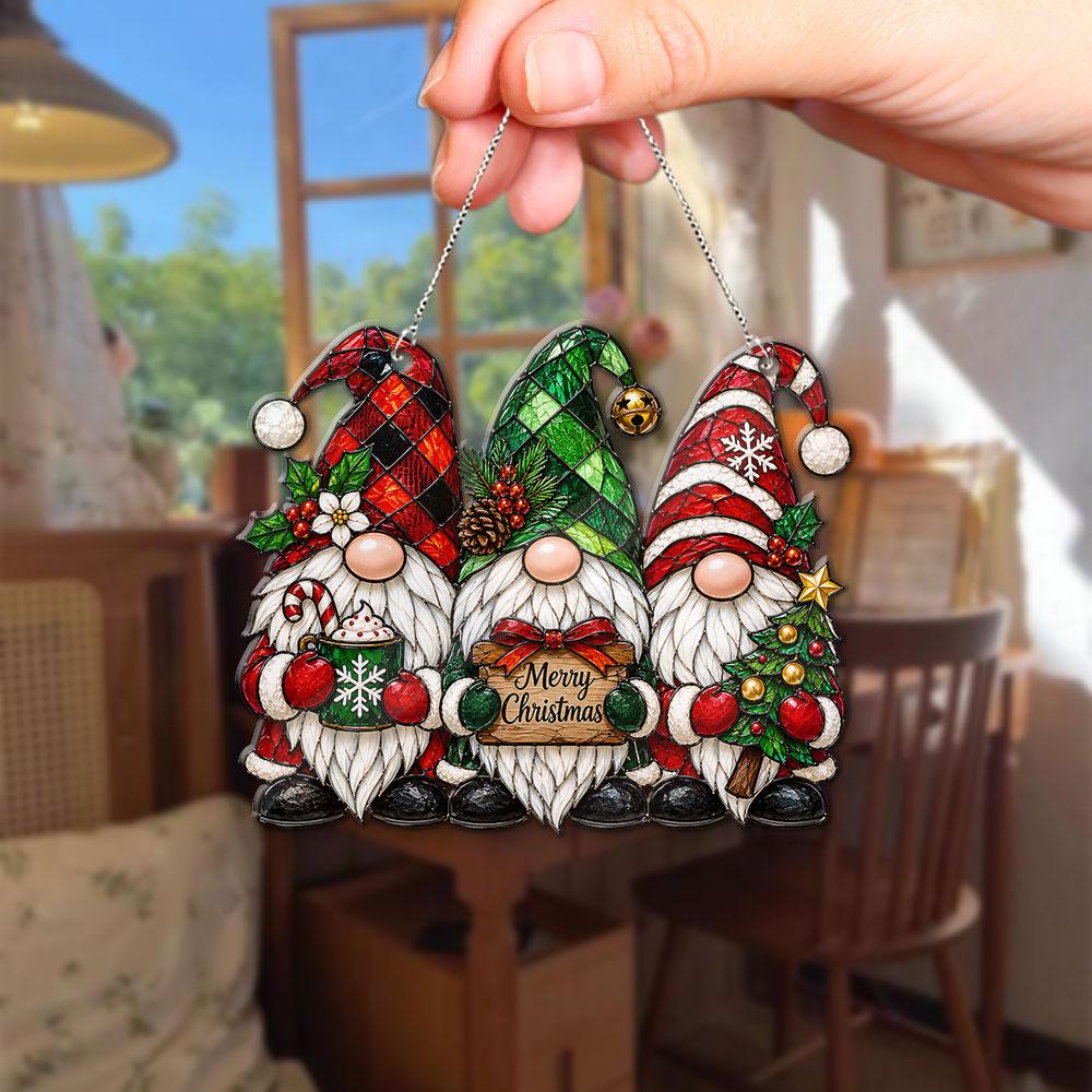 May include: A hanging Christmas ornament featuring three gnomes with white beards. The left gnome wears a red plaid hat, the center gnome a green plaid hat, and the right gnome a red striped hat. The center gnome holds a sign reading Merry Christmas.