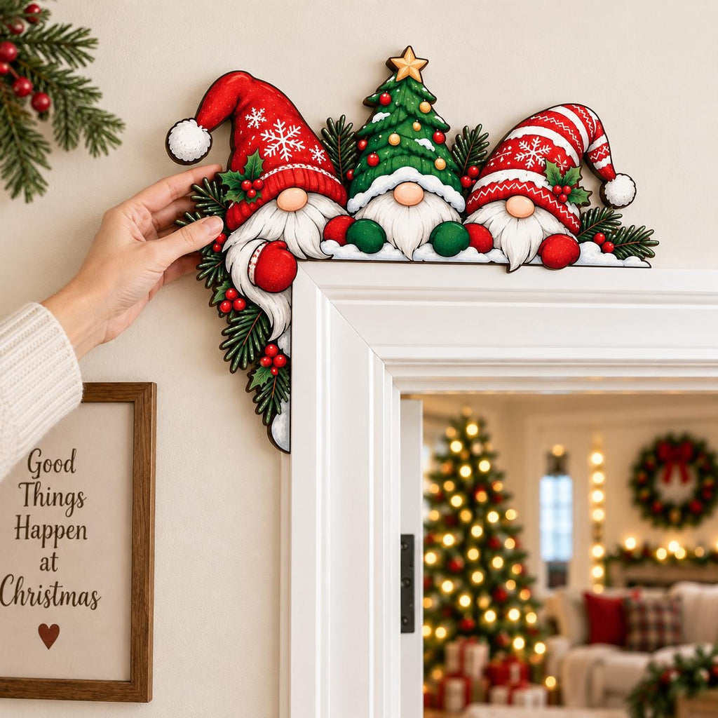May include: A decorative wooden door corner sign featuring two gnomes wearing red and white patterned hats and a central green Christmas tree with a gold star. The design includes green pine branches and red berries, positioned on a white door frame.