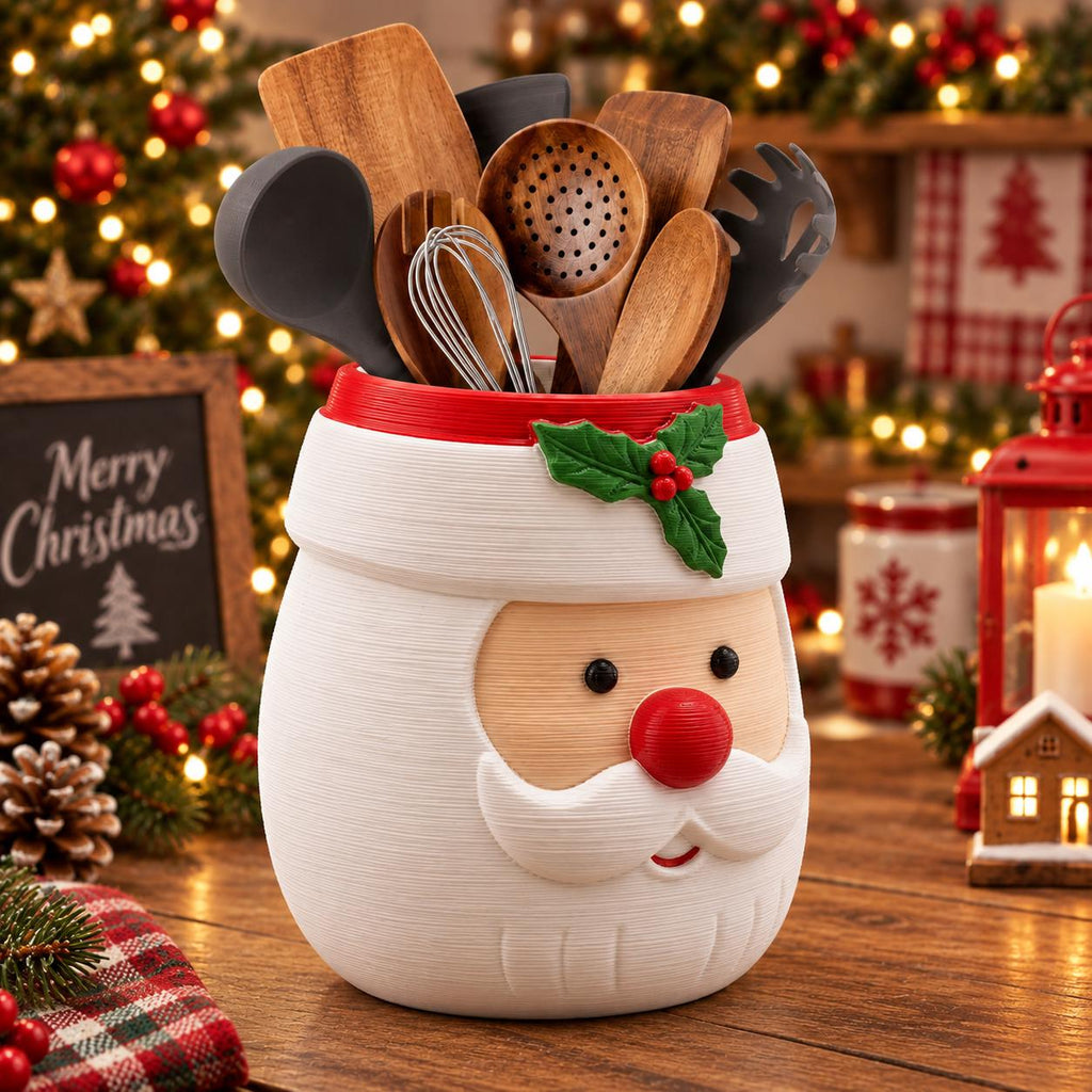 May include: A white ceramic utensil holder shaped like a Santa Claus face with a red rim, featuring a green holly leaf and red berry accent. The container is filled with various kitchen tools, including wooden spoons, a whisk, and black silicone utensils.