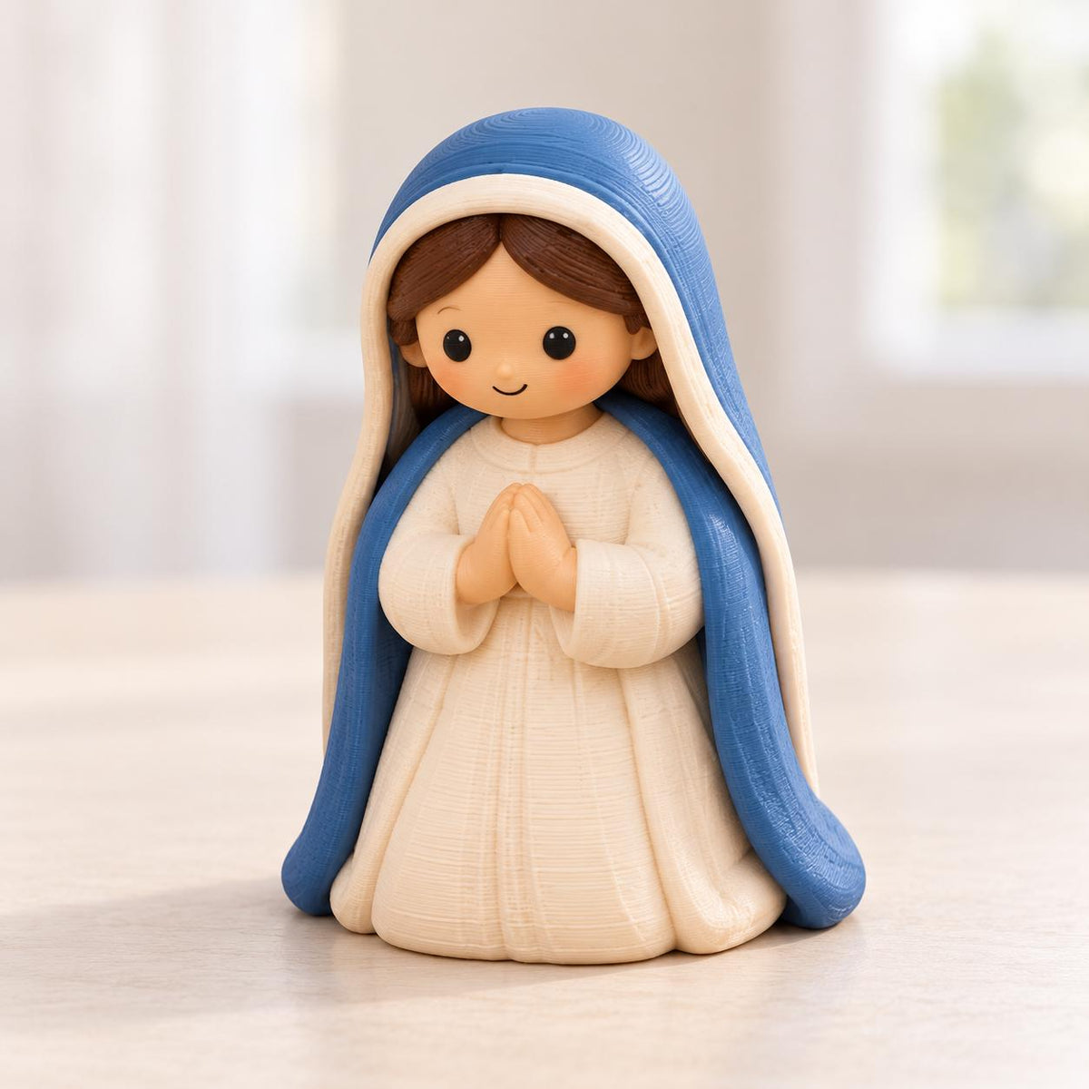 May include: A small figurine of a person with brown hair, wearing a white dress and a blue head covering. The figure has a light skin tone, black eyes, and a small smile, with hands pressed together in a prayer position at the chest.
