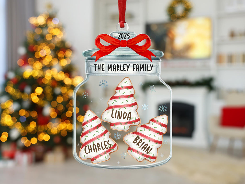 May include: A clear glass jar ornament featuring a red ribbon at the top with the year 2025. The jar is labeled The Marley Family and contains three tree-shaped cookies decorated with red stripes, green sprinkles, and the names Charles, Linda, and Brian.