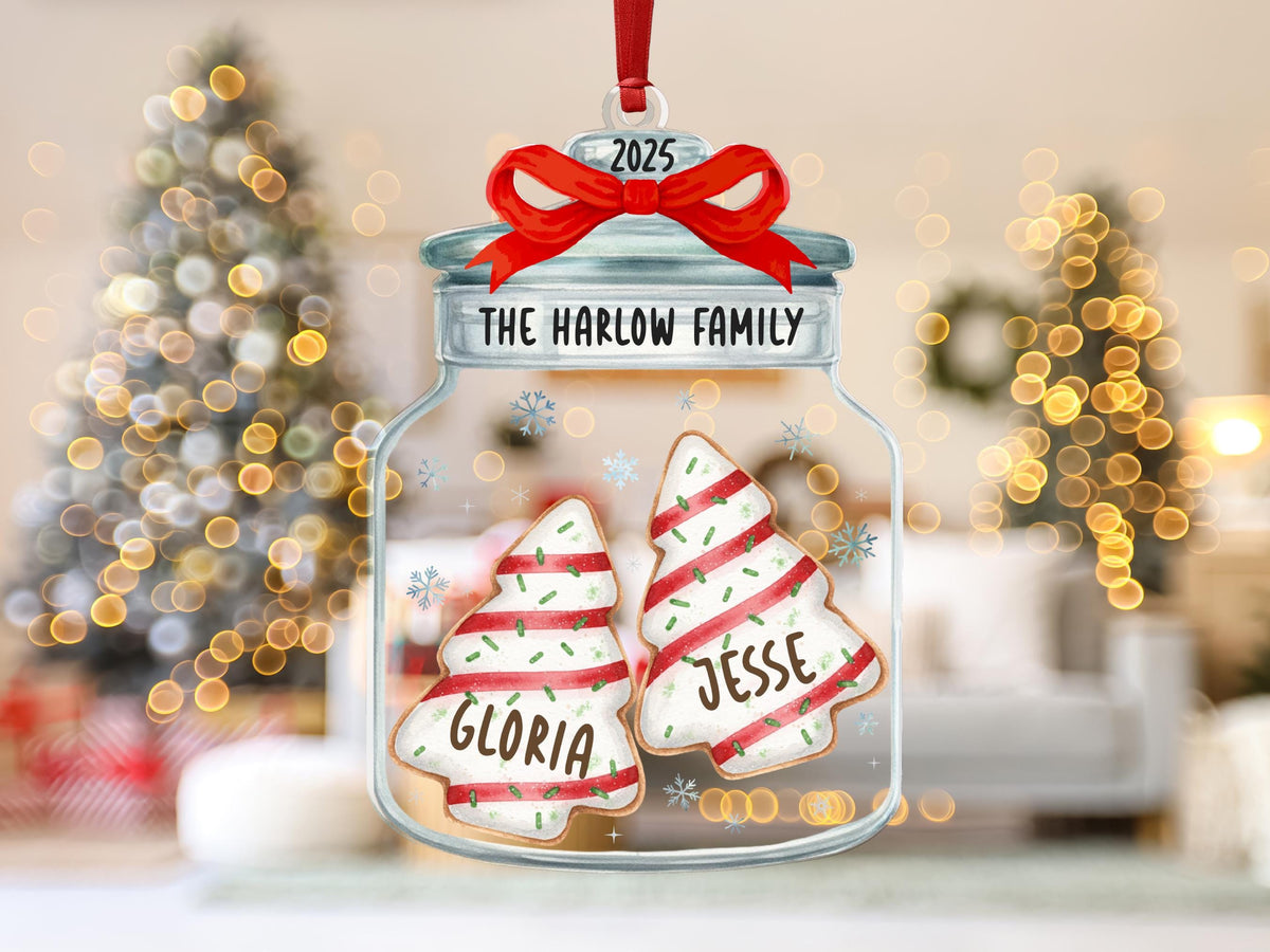 May include: A clear glass jar ornament featuring a red ribbon bow at the top with the year 2025. The jar is labeled The Harlow Family and contains two tree-shaped cookies decorated with red stripes, green sprinkles, and the names Gloria and Jesse.