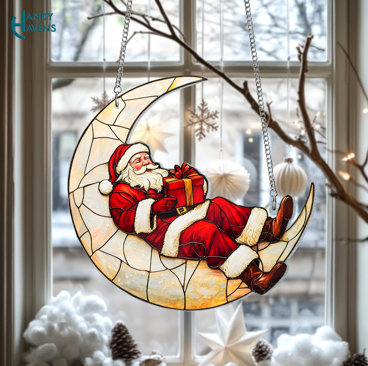 May include: A stained glass Christmas decoration featuring Santa Claus reclining on a crescent moon. Santa wears a red suit with white trim and holds a wrapped gift. The moon is a light yellow color, and the decoration hangs from a silver chain.