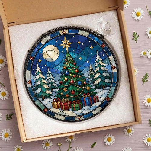 May include: A circular stained glass suncatcher featuring a decorated Christmas tree, snow-covered pine trees, and wrapped gifts under a starry night sky with a large moon. The piece is framed in black metal and includes a clear suction cup hook.