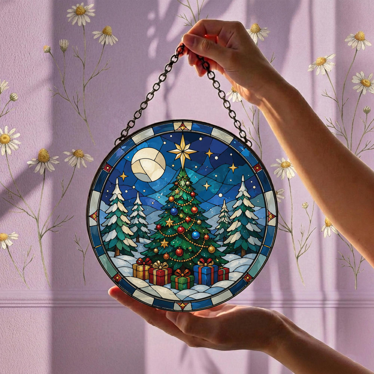May include: A circular stained glass suncatcher featuring a decorated Christmas tree with colorful ornaments and gifts underneath, set against a snowy landscape with a bright star and a moon in a deep blue night sky, suspended by a black metal chain.