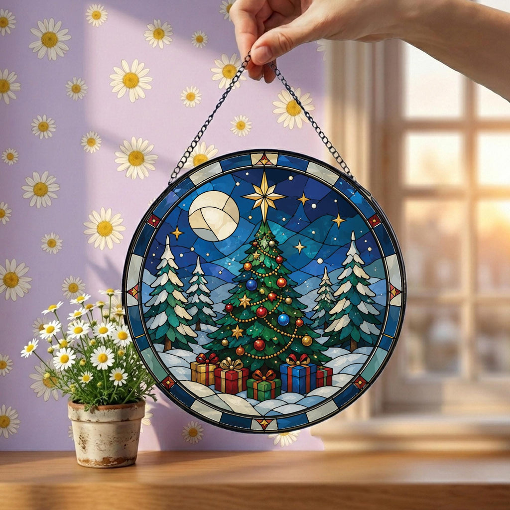 May include: A circular stained glass suncatcher featuring a winter scene with a decorated Christmas tree, wrapped gifts, and a full moon against a dark blue sky. The piece is framed in a dark border and hangs from a thin metal chain.