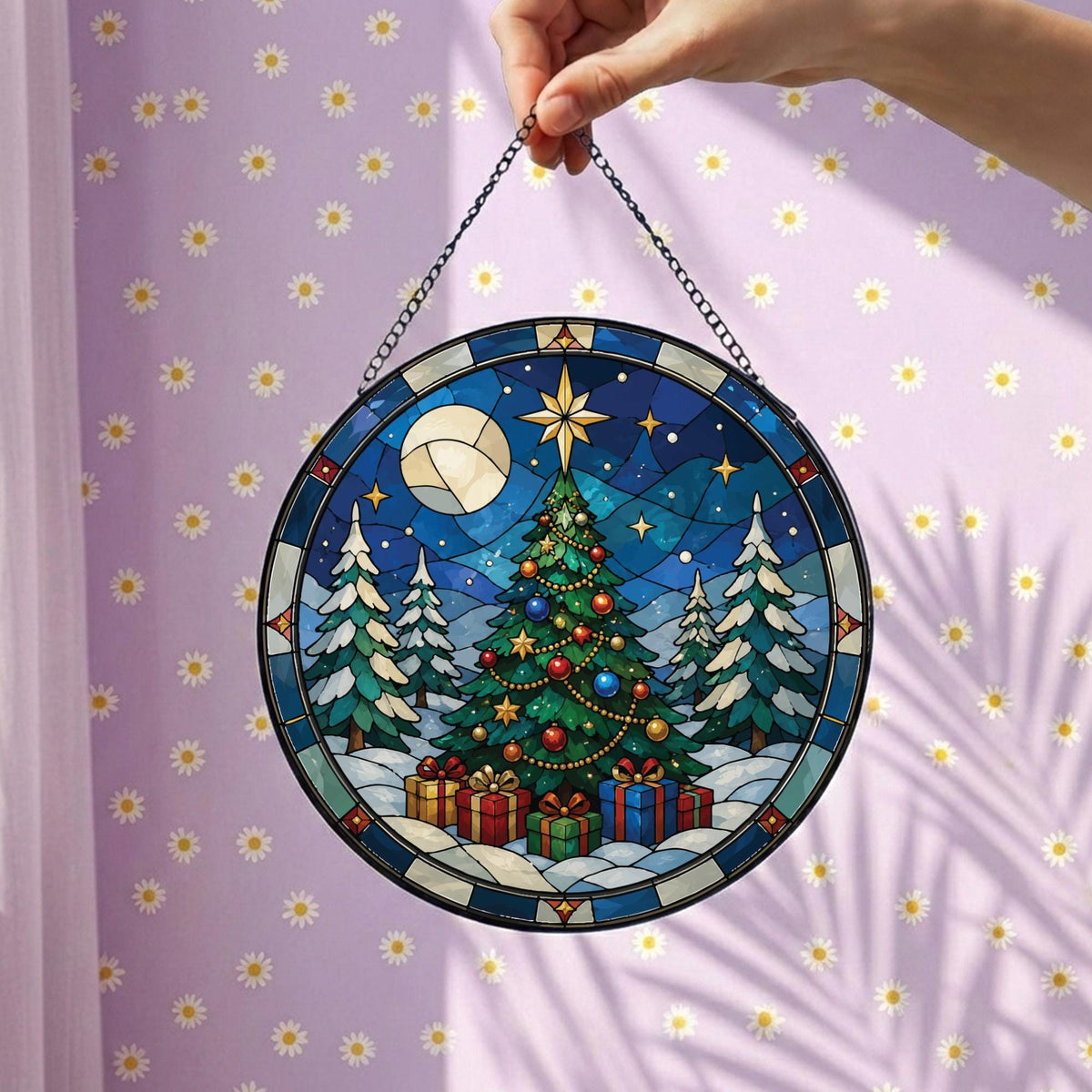 May include: A circular stained glass suncatcher featuring a Christmas tree decorated with colorful ornaments and a star topper. The scene includes snow-covered pine trees, wrapped gifts at the base, and a moon in a dark blue night sky.