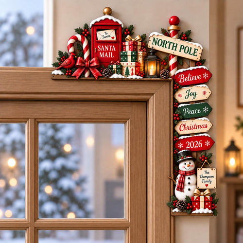 May include: A wooden Christmas door corner sign featuring a red Santa mail box, a candy cane, a cardinal, stacked gift boxes, and a lantern. A vertical sign post displays North Pole, Believe, Joy, Peace, Christmas, 2026, and a snowman with a sign.