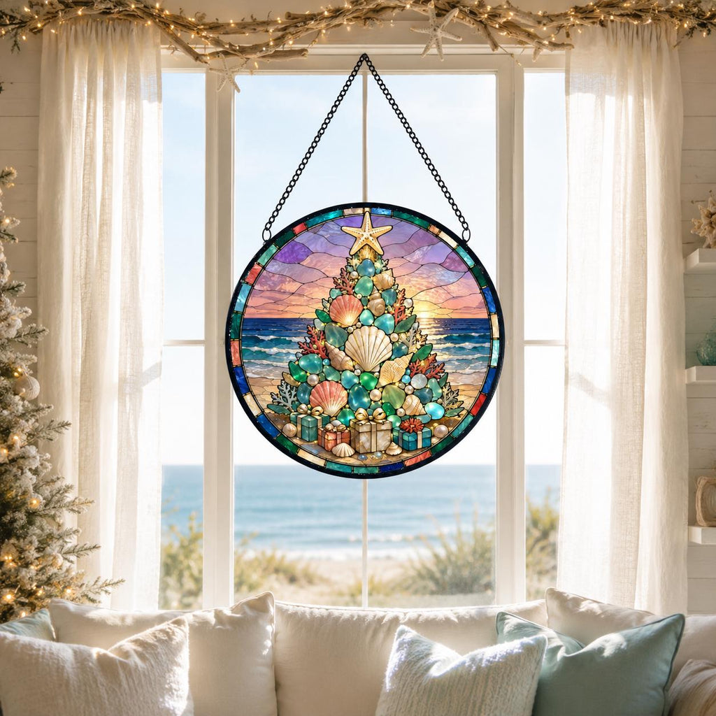 May include: A circular stained glass suncatcher featuring a Christmas tree composed of various seashells, coral, and pearls. The tree is topped with a starfish and sits on a beach with a sunset ocean horizon. It hangs from a black metal chain.