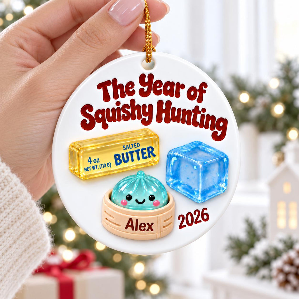 May include: A round white ceramic ornament featuring the red text The Year of Squishy Hunting, a yellow stick of salted butter, a blue ice cube, and a teal dumpling in a bamboo steamer with the name Alex and the year 2026 printed on the surface.