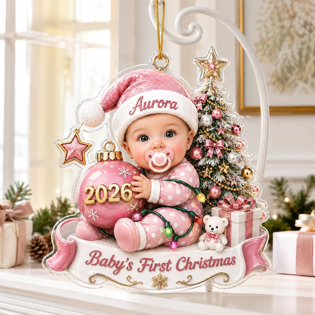 May include: A hanging Christmas ornament featuring a baby wearing a pink hat with the name Aurora, holding a pink ornament labeled 2026. The scene includes a decorated tree, a small teddy bear, and a banner reading Baby's First Christmas.