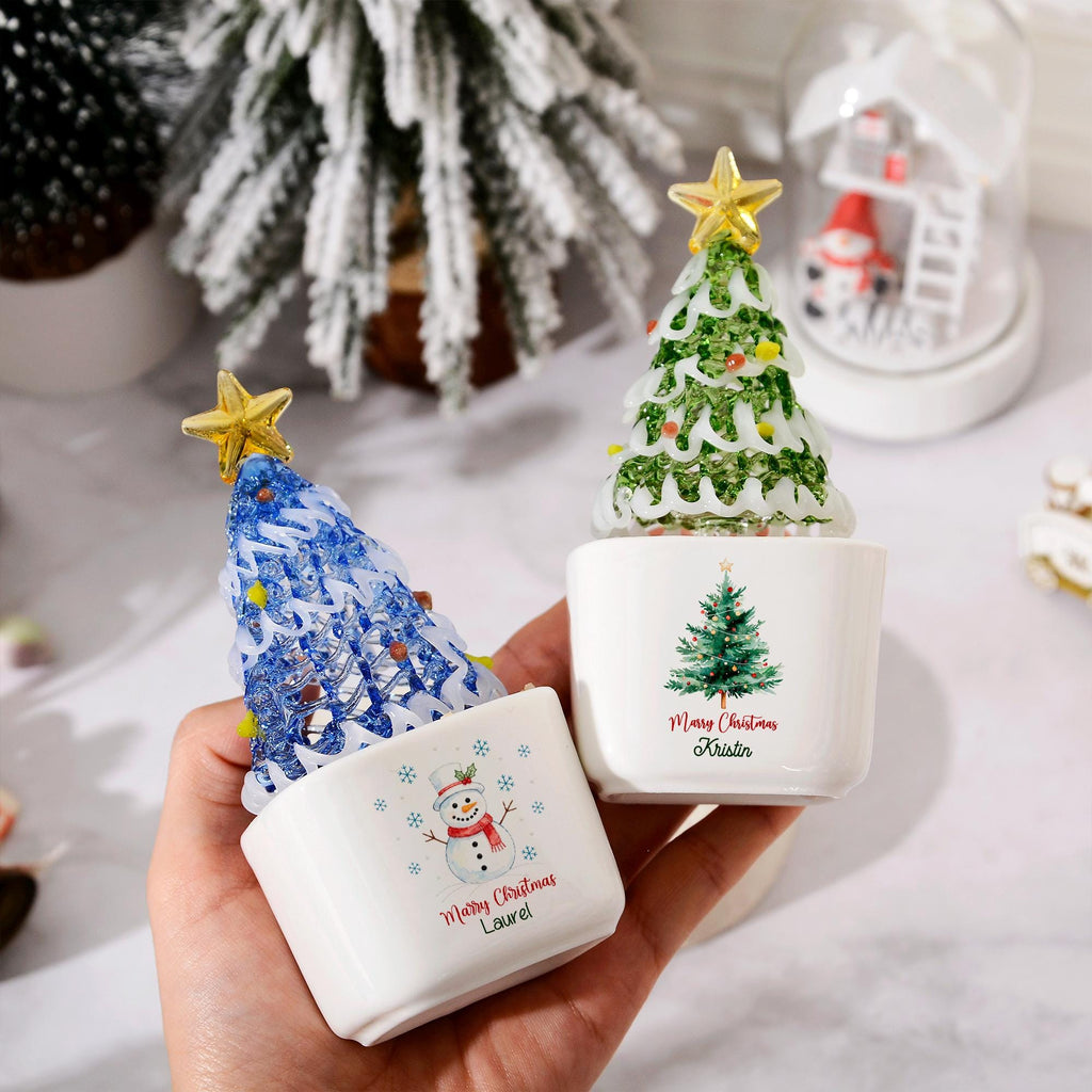 May include: Two white ceramic square planters featuring glass Christmas tree ornaments with gold stars on top. One planter displays a snowman graphic with the text Merry Christmas Laurel, while the other shows a pine tree with Merry Christmas Kristin.