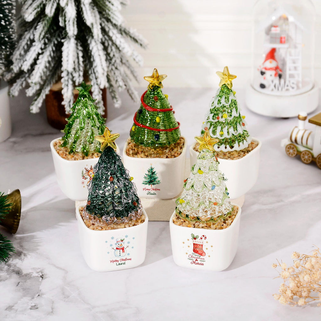 May include: Five miniature Christmas tree ornaments in white square ceramic pots. Each tree is crafted from green or clear wire with colorful beads and a gold star topper. The pots feature festive holiday graphics including a snowman and stocking.