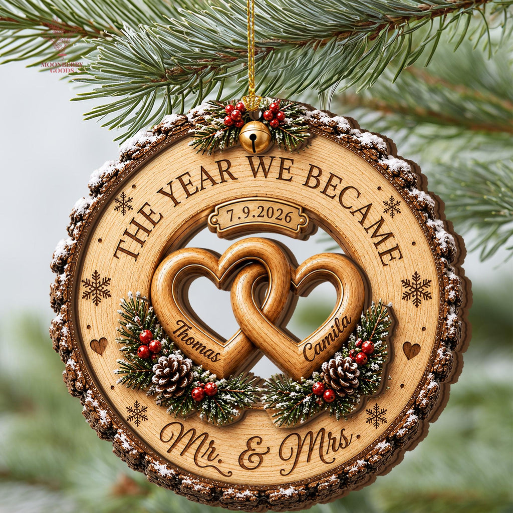 May include: A round wooden Christmas ornament featuring a bark-textured edge with faux snow. It displays two interlocking hearts engraved with the names Thomas and Camila, the text THE YEAR WE BECAME, Mr. & Mrs., and the date 7.9.2026.