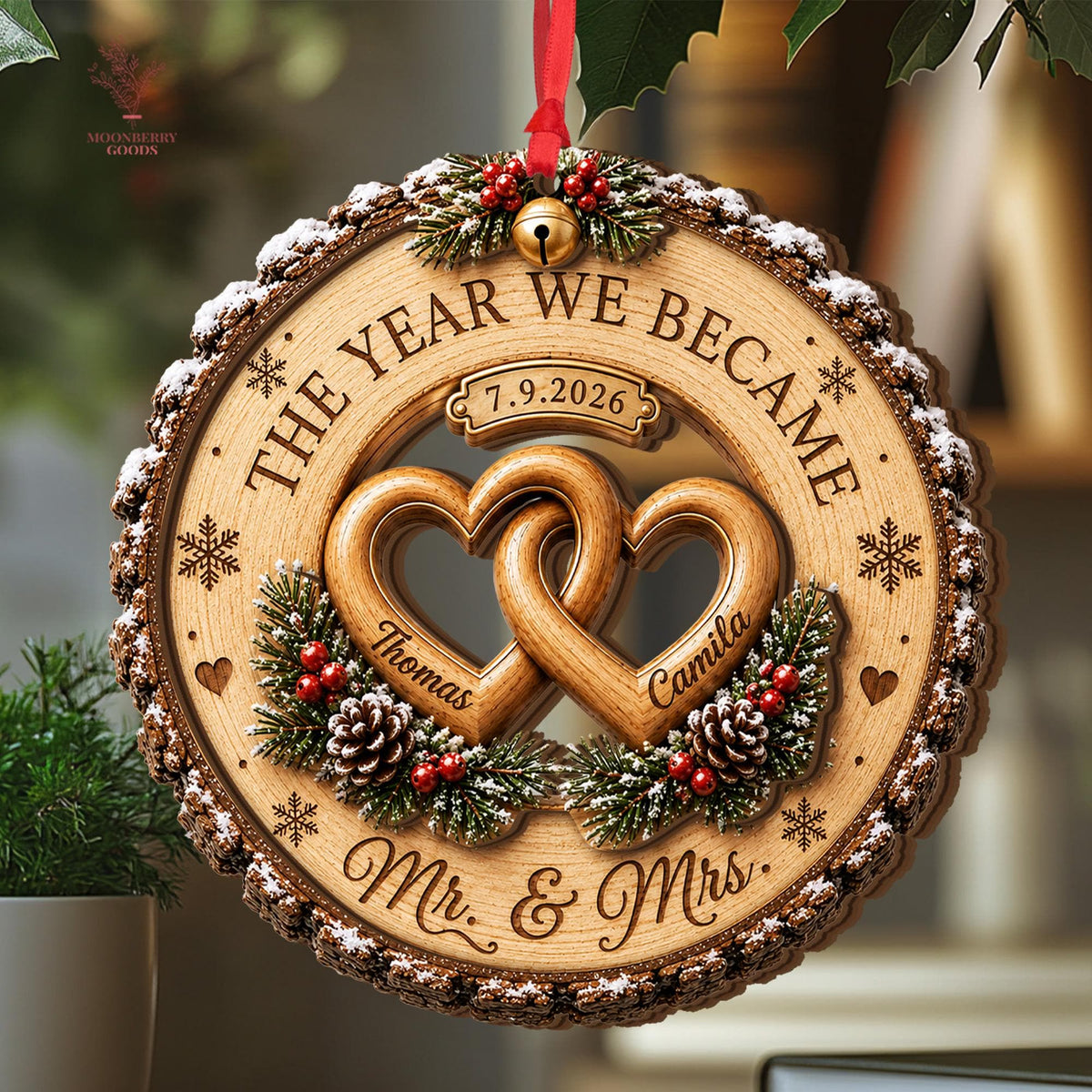 May include: A round wooden ornament featuring two interlocking hearts engraved with the names Thomas and Camila. The text reads THE YEAR WE BECAME, 7.9.2026, and Mr. & Mrs. It is decorated with pine branches, pinecones, red berries, and a gold bell.