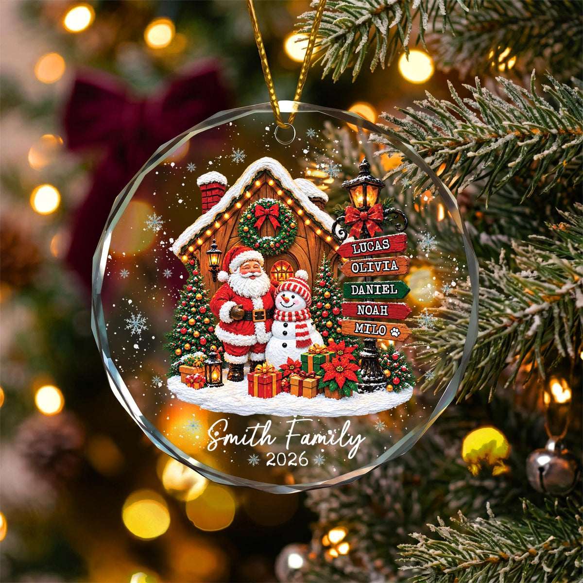 May include: A round, clear glass Christmas ornament featuring a festive scene with Santa Claus and a snowman standing before a snow-covered house. A signpost lists the names Lucas, Olivia, Daniel, Noah, and Milo, with Smith Family 2026 below.