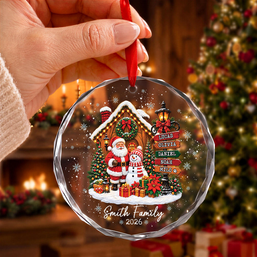 May include: A round, clear Christmas ornament featuring a printed scene of Santa Claus and a snowman in front of a cabin. A signpost lists the names Lucas, Olivia, Daniel, Noah, and Milo. The text Smith Family 2026 is printed at the bottom.