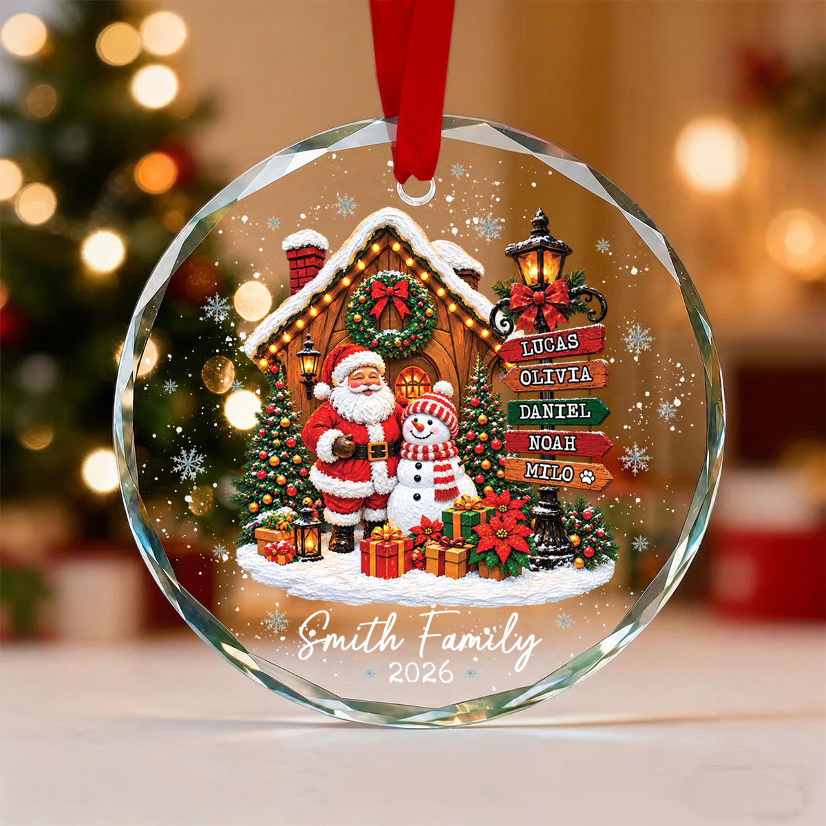 May include: A round, clear glass Christmas ornament with a red ribbon hanger. The design features Santa Claus and a snowman in front of a cabin, a street sign with the names Lucas, Olivia, Daniel, Noah, and Milo, and the text Smith Family 2026.