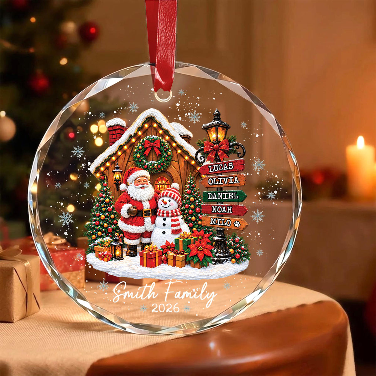 May include: A circular clear glass Christmas ornament featuring a printed scene of Santa Claus and a snowman in front of a cabin. A signpost lists the names Lucas, Olivia, Daniel, Noah, and Milo. The text Smith Family 2026 is printed below.