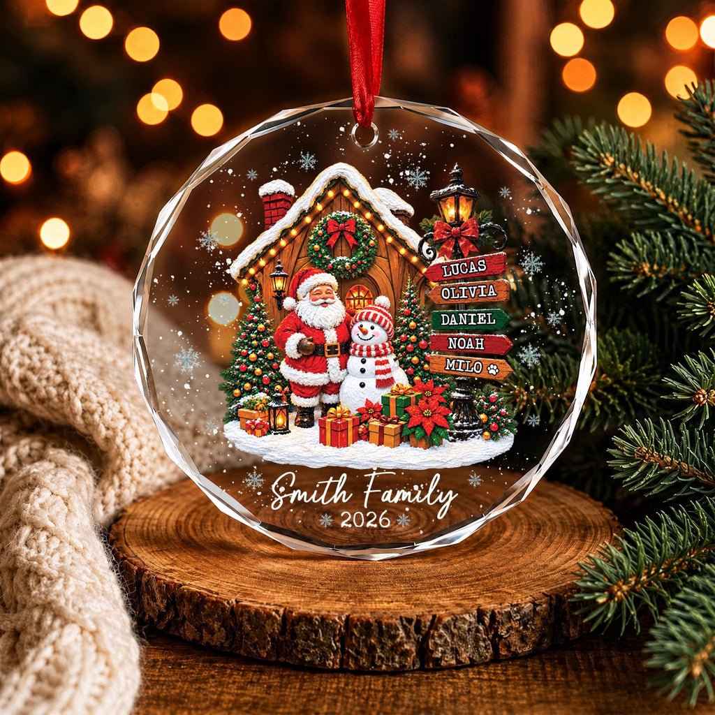 May include: A round, faceted glass Christmas ornament featuring a printed scene of Santa Claus and a snowman in front of a house. A signpost lists the names Lucas, Olivia, Daniel, Noah, and Milo. The text Smith Family 2026 is printed at the bottom.