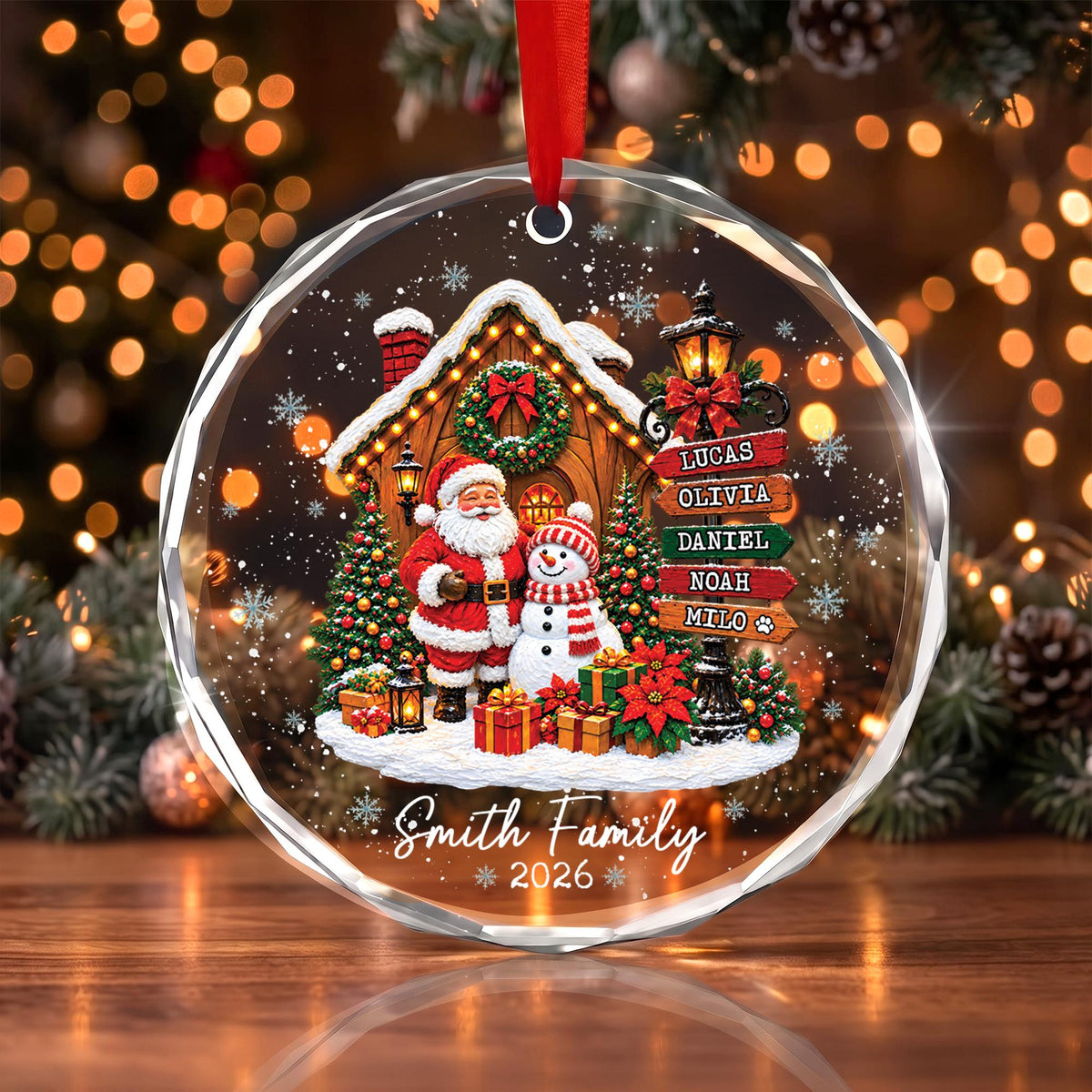 May include: A round, clear acrylic Christmas ornament featuring a festive scene with Santa Claus and a snowman in front of a house. A signpost lists the names Lucas, Olivia, Daniel, Noah, and Milo. The text Smith Family 2026 is printed below.