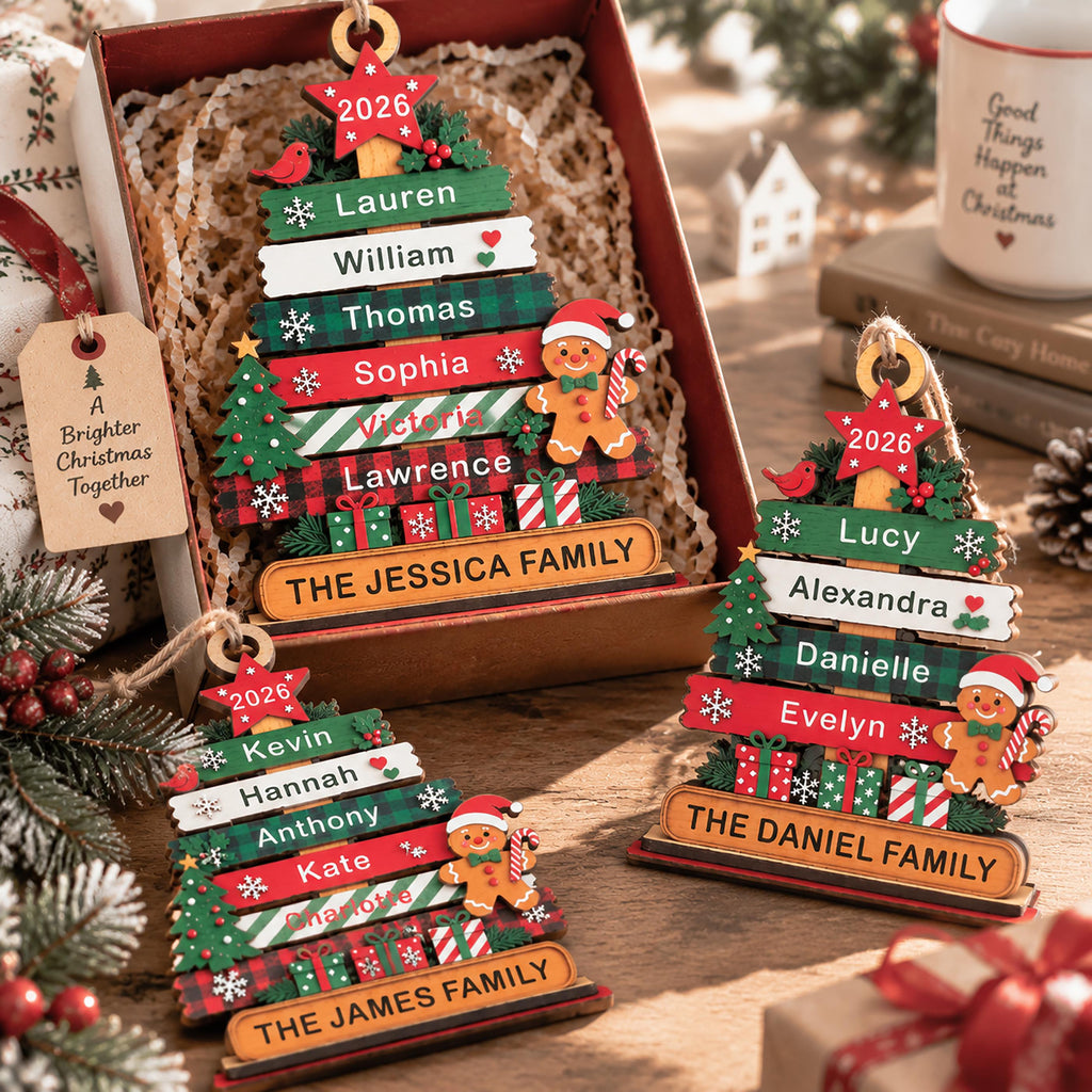 May include: Three wooden Christmas tree ornaments featuring horizontal slats with names, a 2026 star topper, and a gingerbread person. Each ornament displays a family name at the base, including The Jessica Family, The Daniel Family, and The James Family.