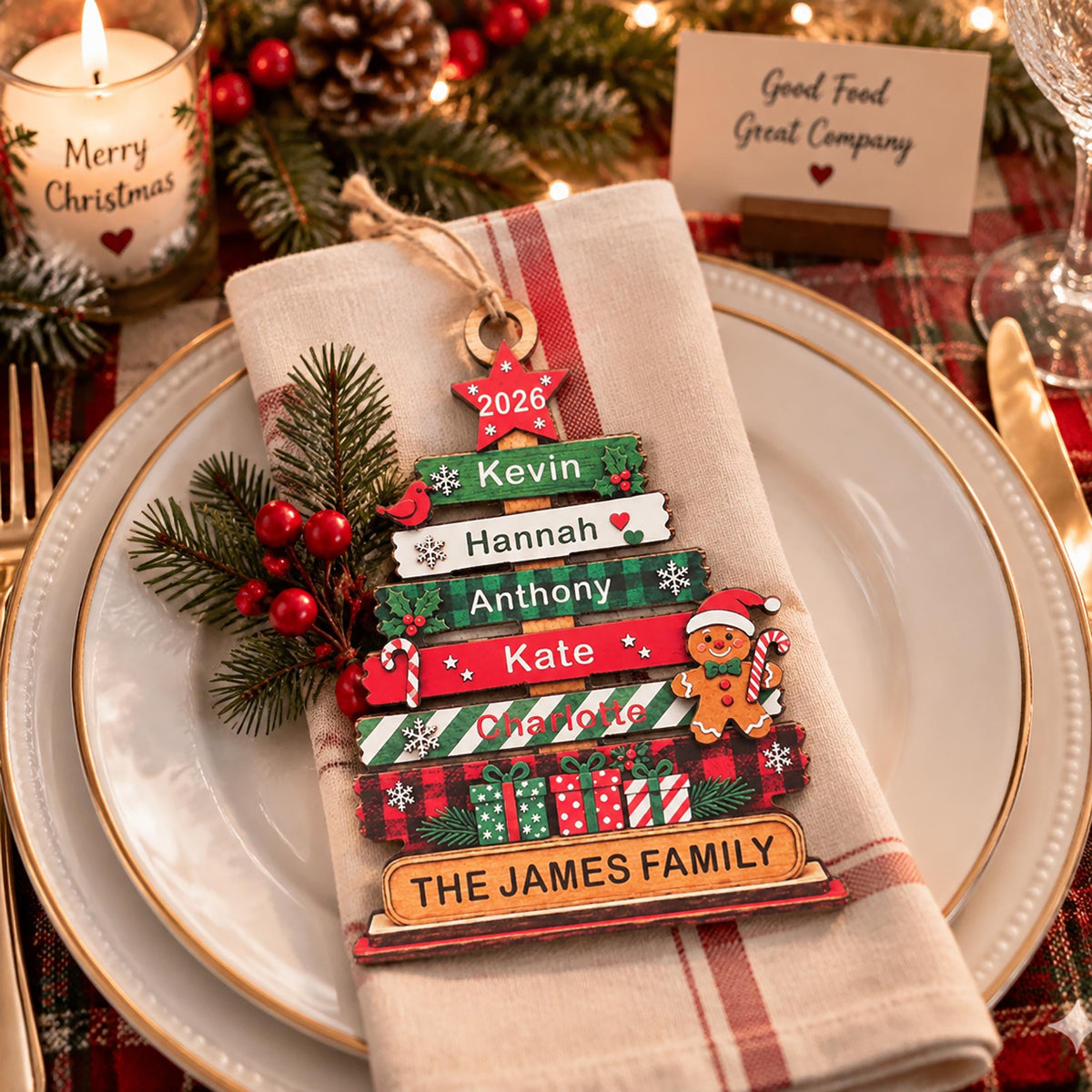 May include: A wooden Christmas tree ornament featuring horizontal slats with the names Kevin, Hannah, Anthony, Kate, and Charlotte, topped with a 2026 star. The base displays The James Family, decorated with a gingerbread man and gift boxes.