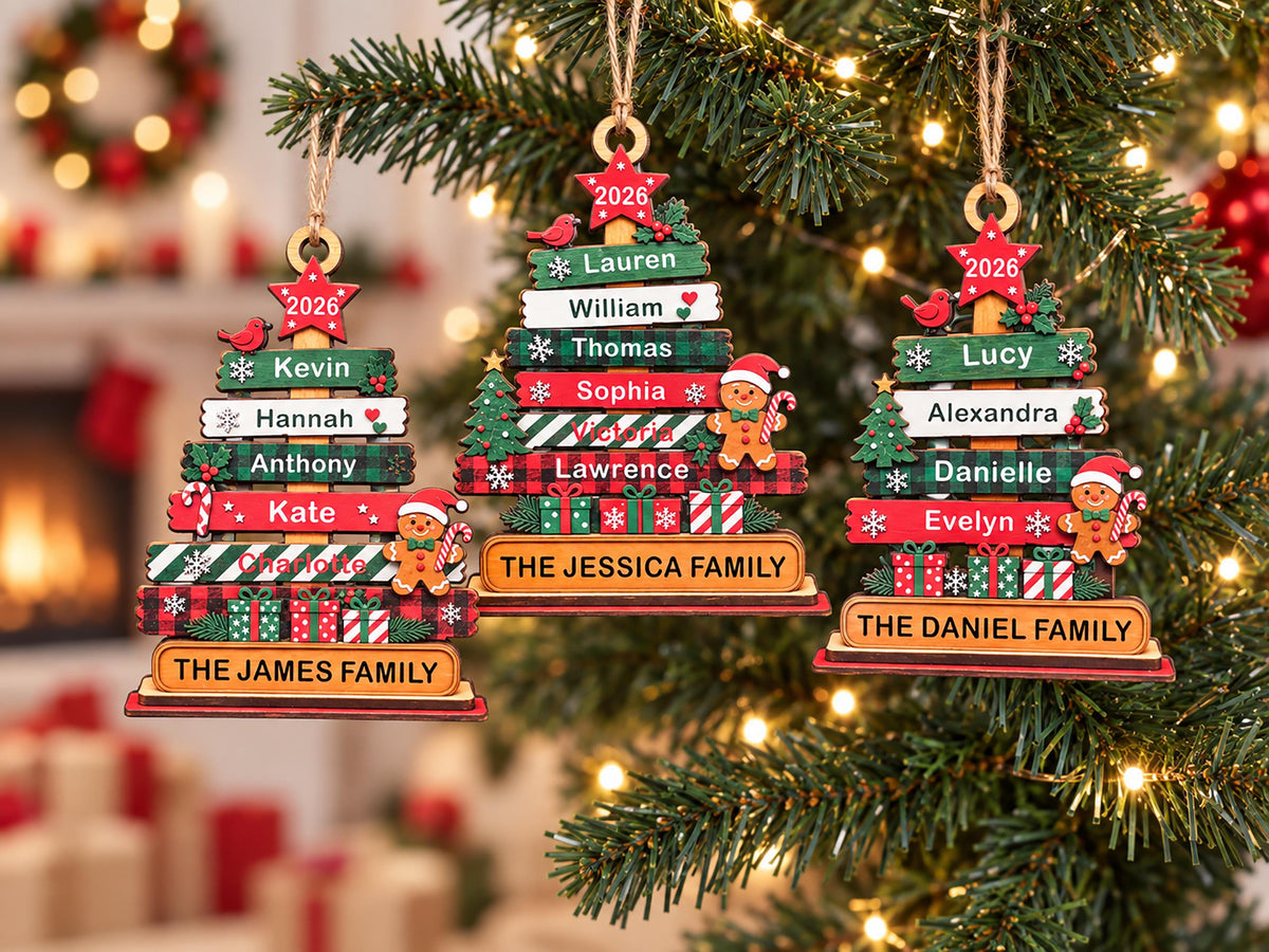 May include: Three wooden Christmas tree ornaments featuring stacked horizontal planks with names, the year 2026 on a red star, and gingerbread figures. The ornaments are labeled THE JAMES FAMILY, THE JESSICA FAMILY, and THE DANIEL FAMILY in black text.
