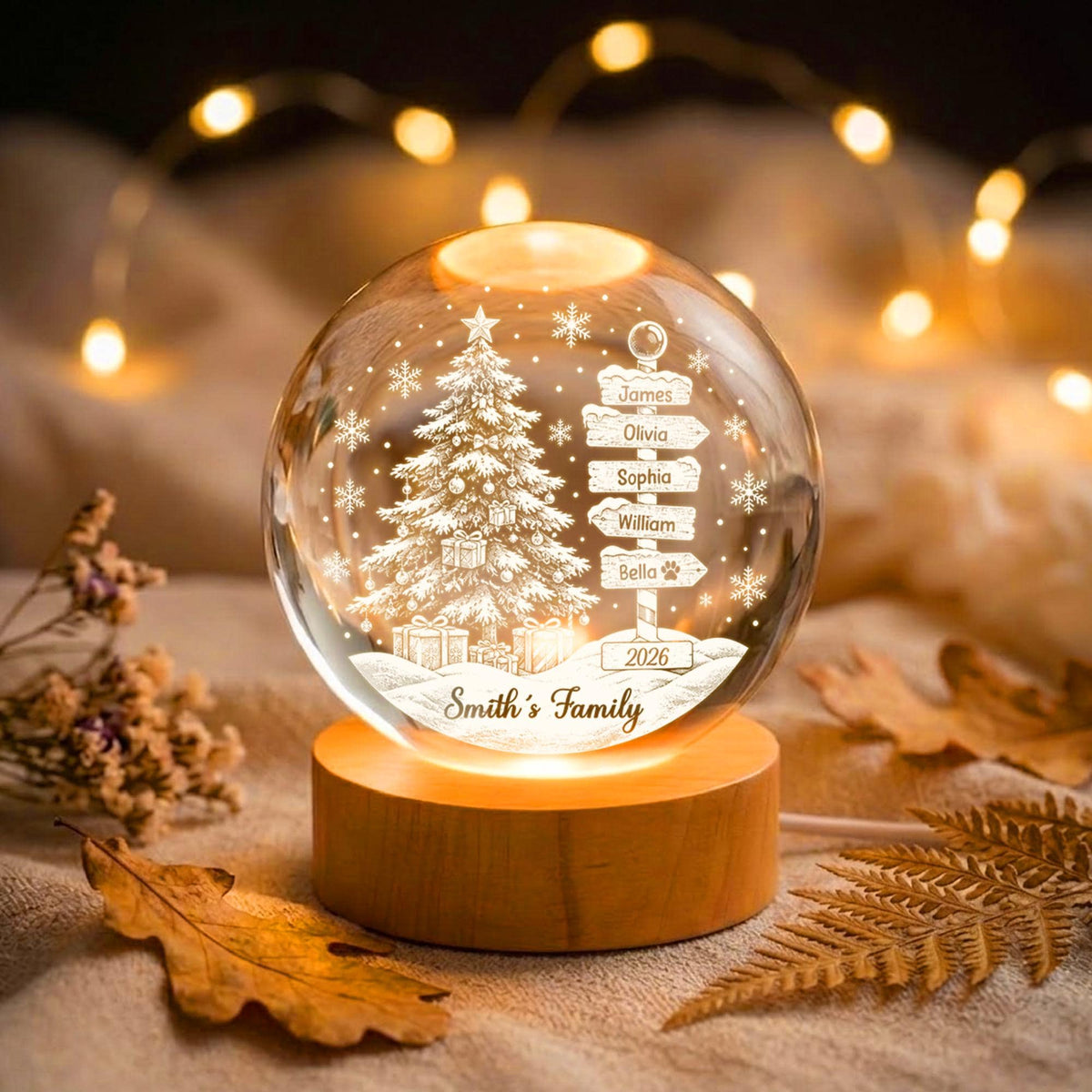 May include: A clear glass sphere night light on a round wooden base. The sphere features an etched design of a Christmas tree, snowflakes, and a signpost with the names James, Olivia, Sophia, William, Bella, the year 2026, and Smith's Family.