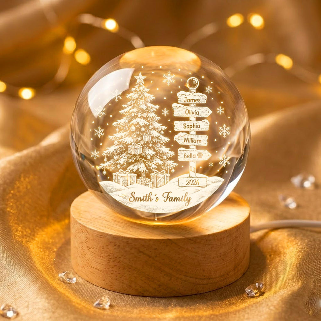 May include: A clear glass sphere ornament featuring an etched Christmas tree, snowflakes, and a signpost with the names James, Olivia, Sophia, William, and Bella, plus the year 2026 and the text Smith's Family, mounted on a round wooden base.