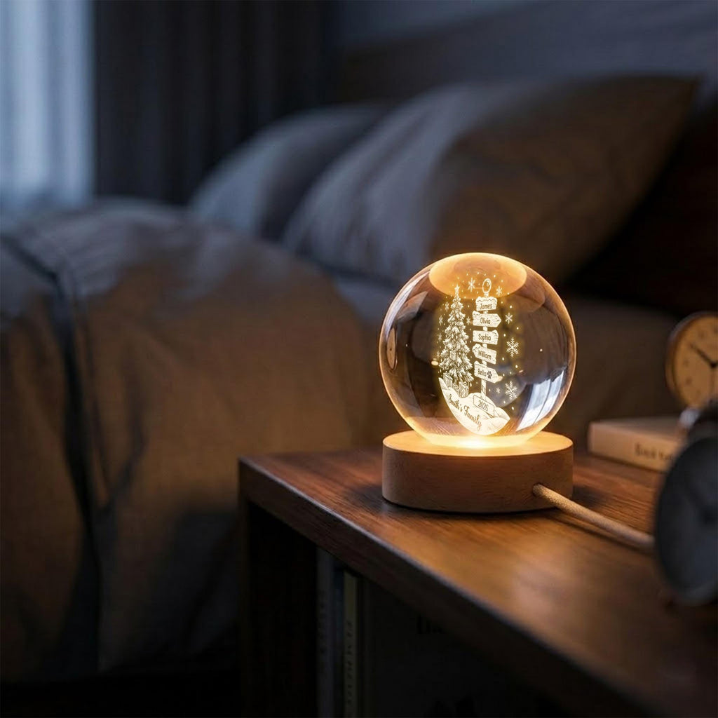 May include: A spherical glass night light featuring an internal 3D laser-etched design of a Christmas tree, a signpost with names, and snowflakes. The orb rests on a circular wooden base with a power cord extending from the side, emitting a warm glow.